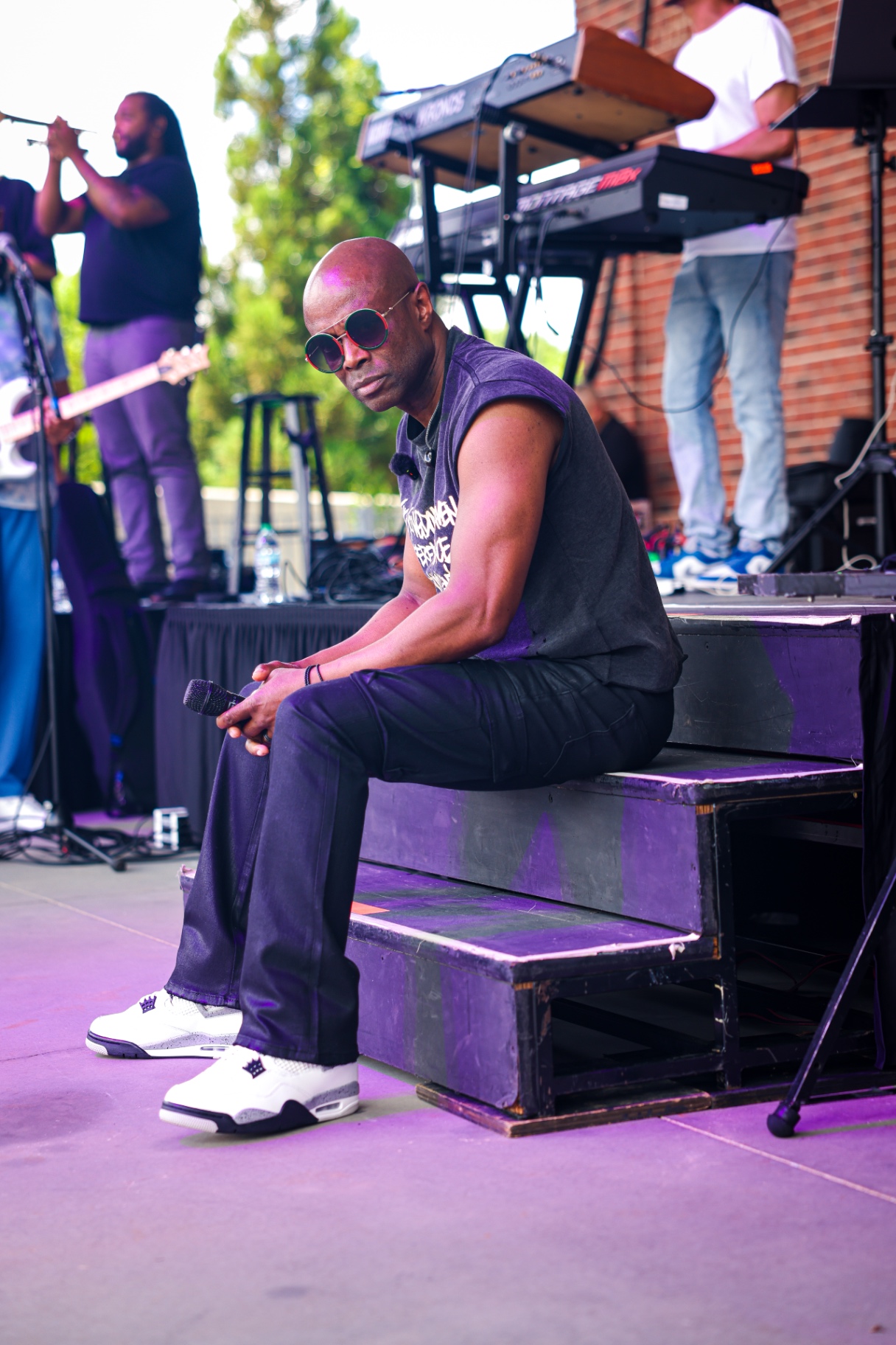 Host seated on stage steps at an outdoor concert